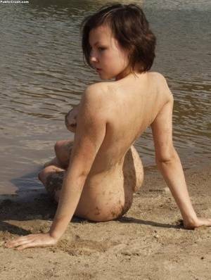 Amateur girl covers her naked body in sand while at a nude beach on adultfans.net