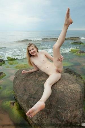 Slim teen Nimfa removes a black bikini to pose naked on seaside rocks on adultfans.net