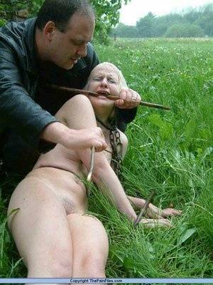 Naked blonde slave is caned and stomped on in a field of lush grass on adultfans.net