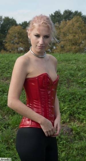 Collared girl Arienh Autumn models a red leather corset while in a field on adultfans.net