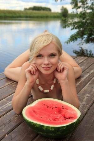 Beautiful blonde Feeona eats a watermelon while posing naked on lakeside dock on adultfans.net