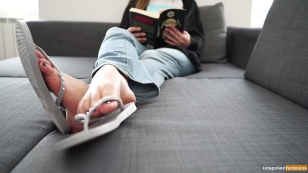 POV foot fetish scene with bare soles in focus while someone reads on the couch on adultfans.net