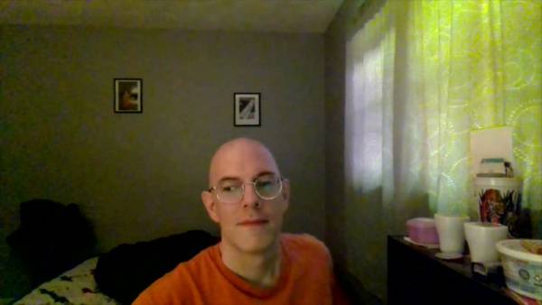Bald man with glasses sits thoughtfully in a softly lit room on adultfans.net