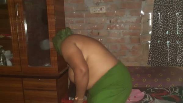 Green-haired stepmom bends over wooden cabinet in bedroom with brick wall on adultfans.net