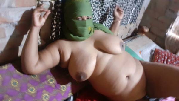 Full-figured woman in a mysterious green mask teases beneath patterned blankets on adultfans.net