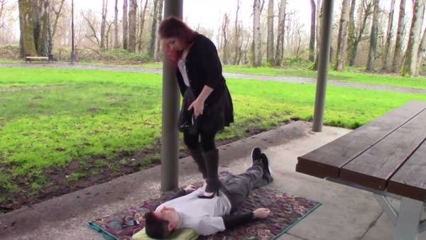 Redhead in heels dominates a man beneath her foot in the park on adultfans.net