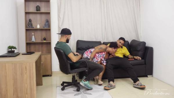 Tattooed woman worships one man while taking another deep from behind on a leather sofa on adultfans.net