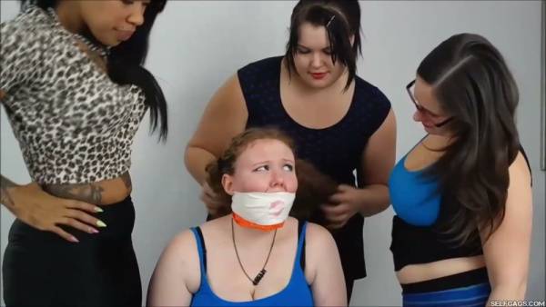 Red-haired woman subdued and gagged by three dominant women in a white room on adultfans.net