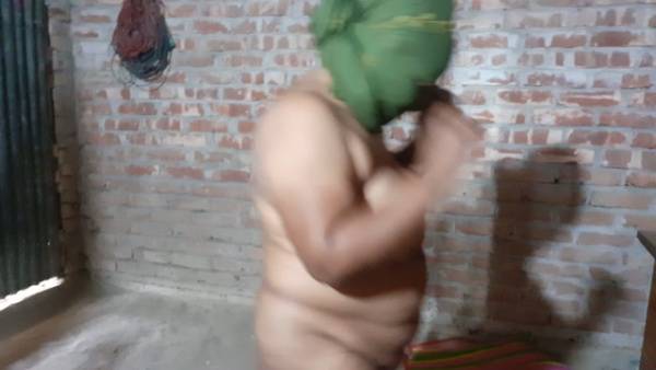 Nude figure in a brick room adjusts green headcloth under dim light on adultfans.net