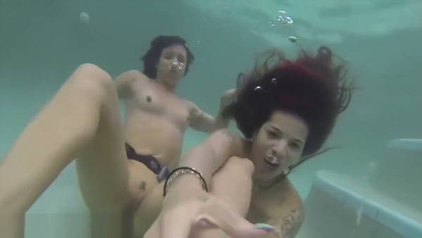 Two women and a man share an intimate underwater moment in a pool with fetish straps on adultfans.net